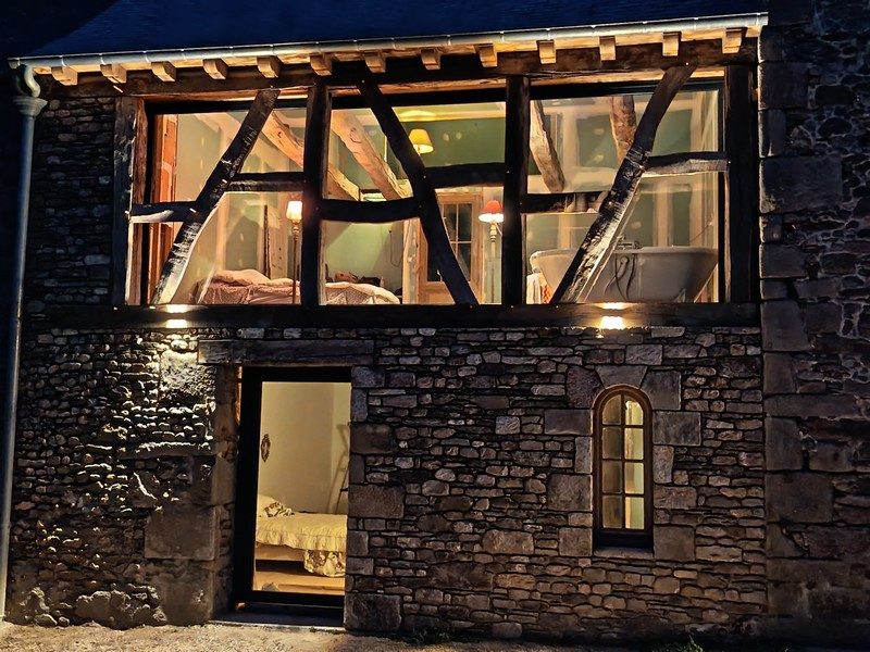 Façade de nuit, porte aluminium anthracite éclairée sous la baie coulissante, mur en pierre