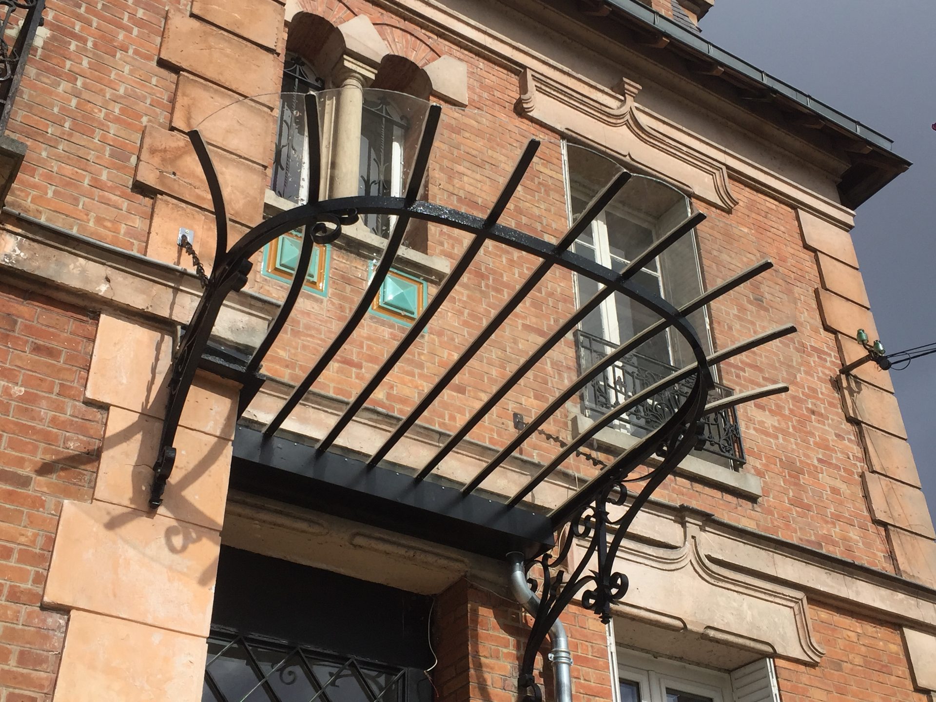 Marquise fer forgé verre trempé Art Nouveau façade brique rouge immeuble