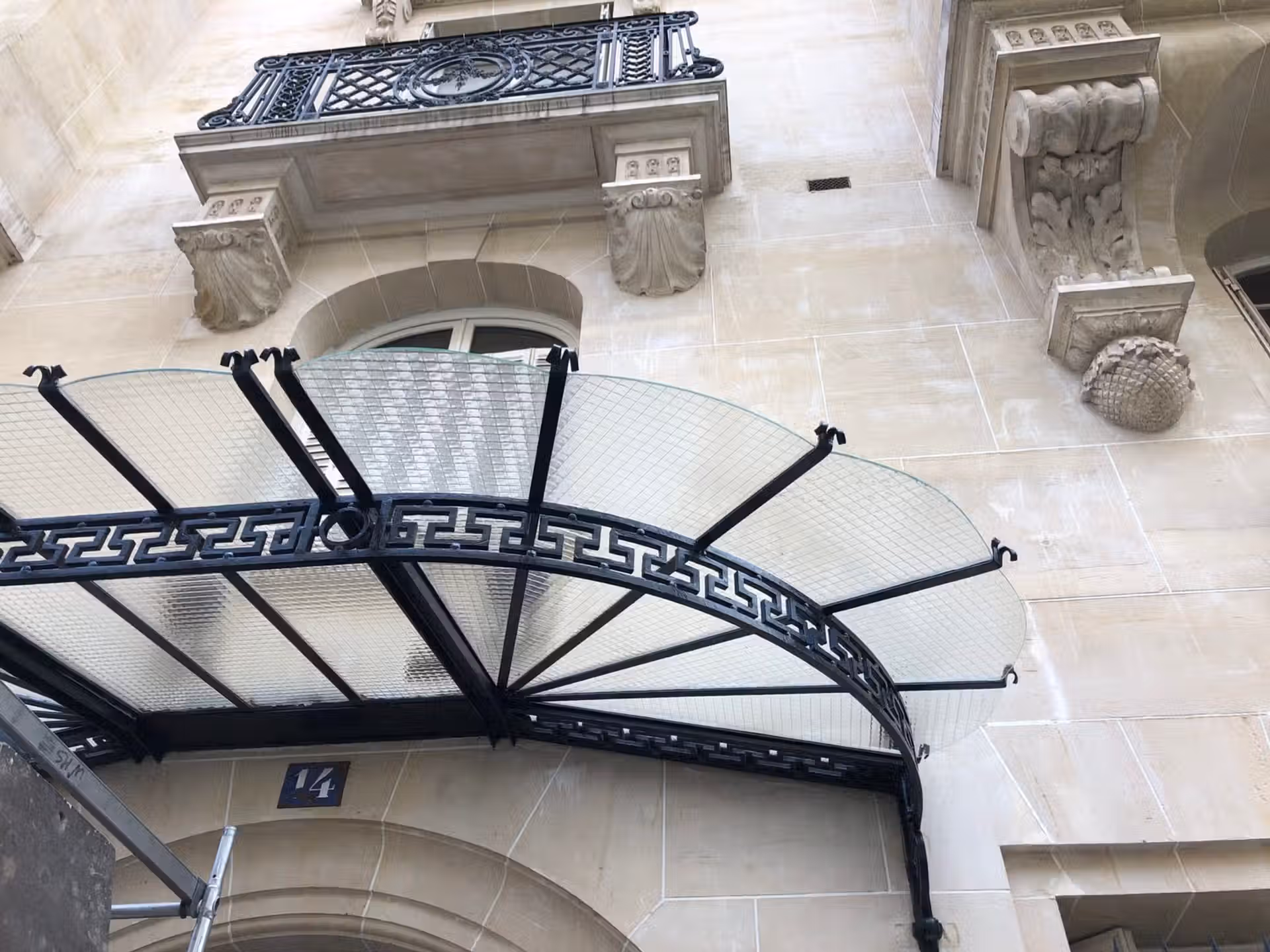 Marquise d'entrée immeuble haussmannien Paris, structure fer forgé noir, vitrage cathédrale quadrillé, ornements sculptés pierre.